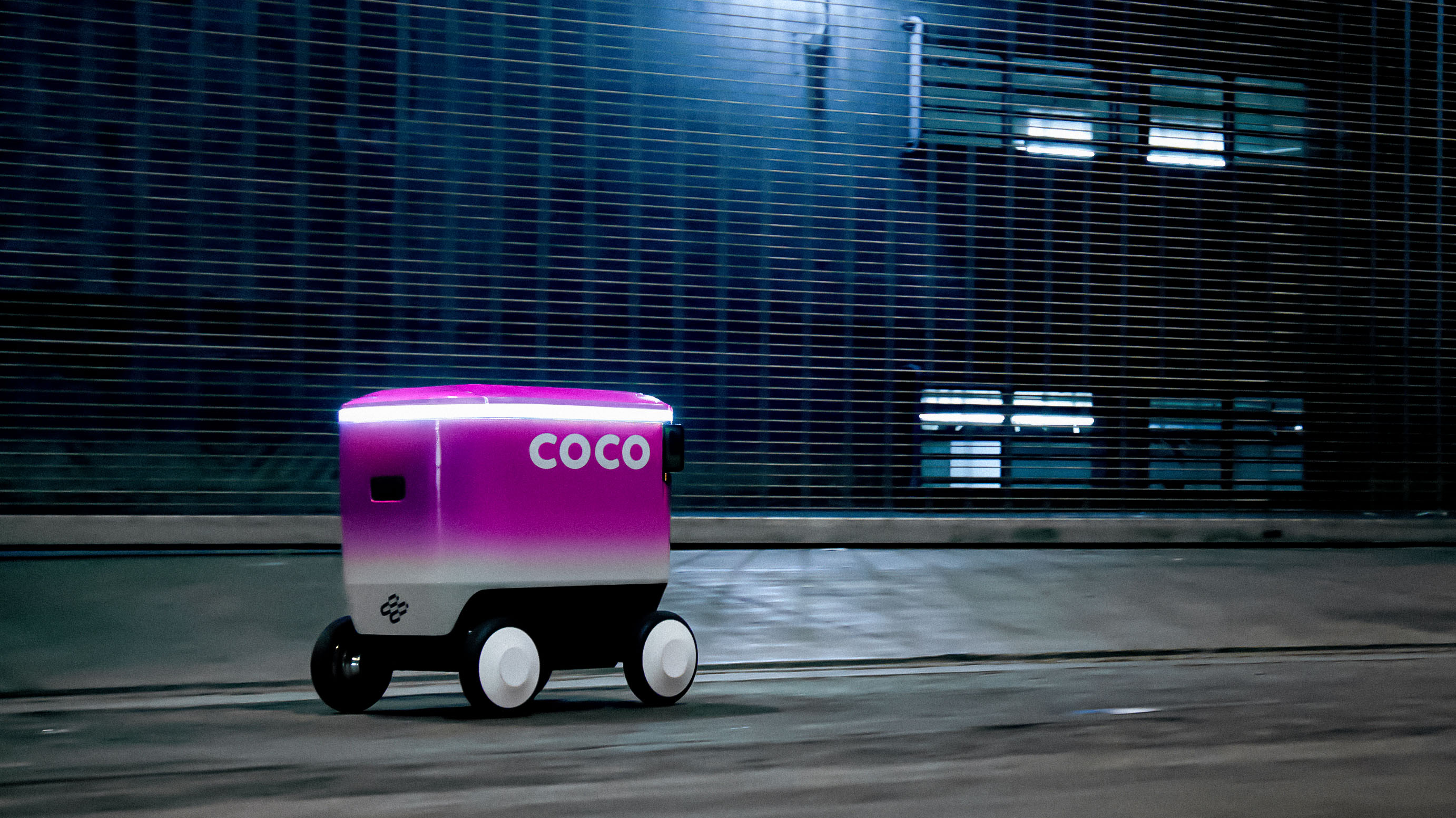a coco robot speeding down a dark city street