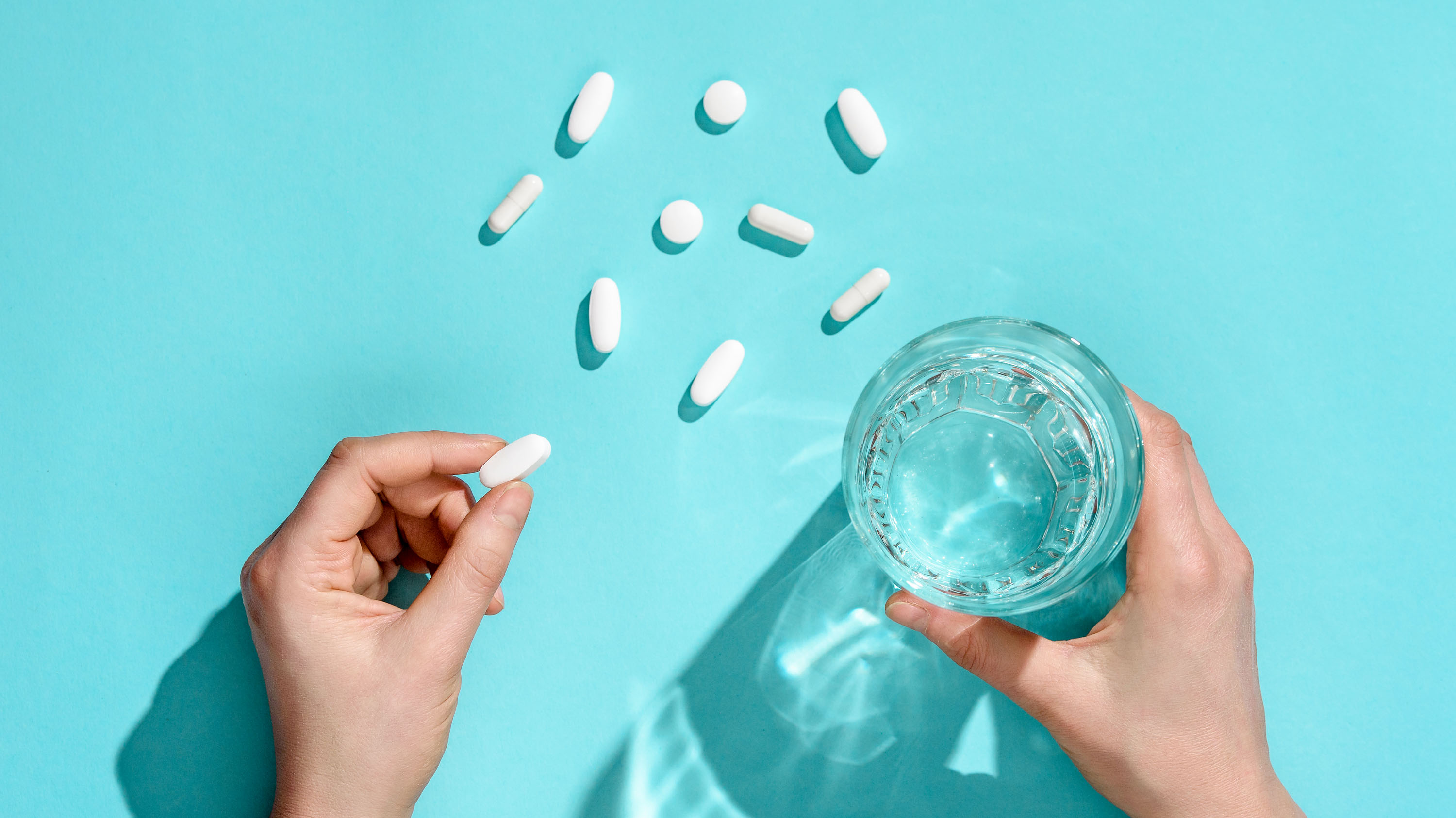 Woman holding in hands white medical pill and glass of water on light blue background